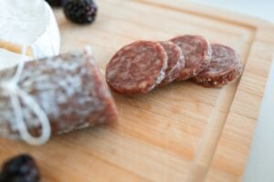 Close-up of an artisanal charcuterie board featuring sliced salami, cheese, and fresh blackberries on a wooden cutting board.